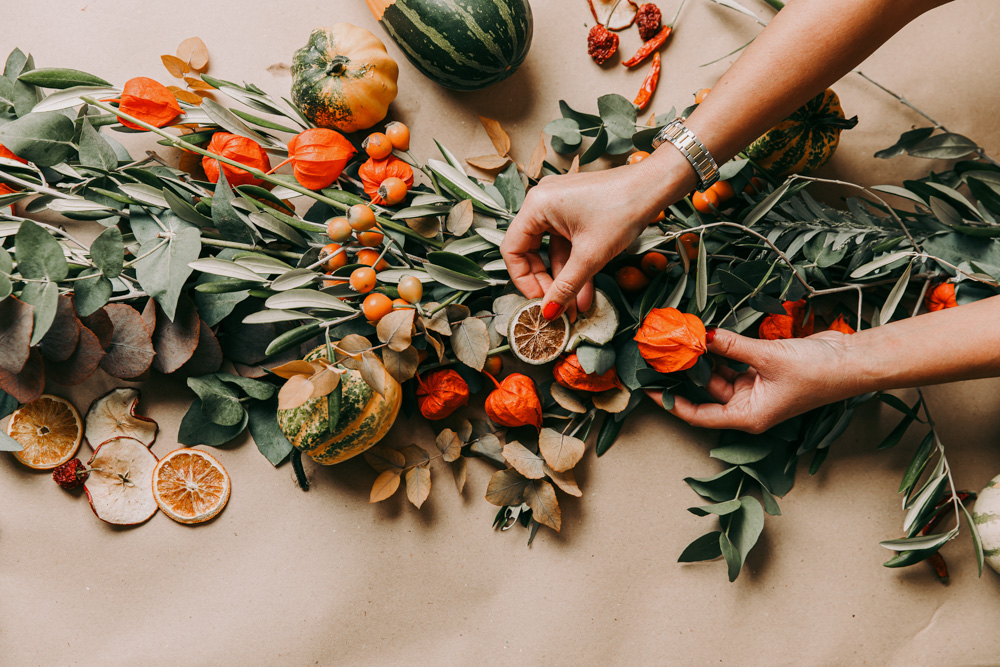 Hands making an autumn garland with leaves and oranges